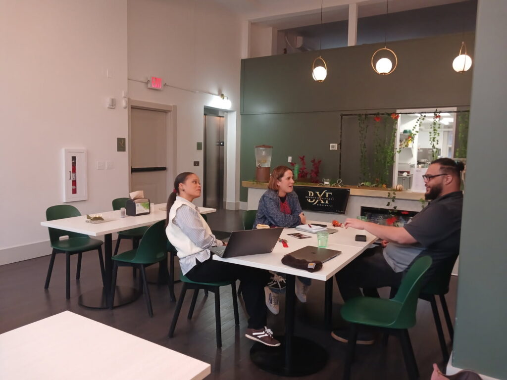 A man sits across from two women laughing. The women are listening intently and smiling.